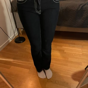 Mörkblå bootcut jeans från true religion  - Snygga mörkblå bootcut jeans från true religion med kontrasterande vita sömmar. De har en lowwaist passform. Jag är 1,70 lång och dom är lite för korta för mig, köpte för 2000kr