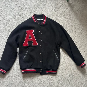 Varsityjacka från Adika - Säljer en svart varsityjacka från ett amerikanskt företag ’Adika’. Jackan har knappar framtill och ribbade muddar i svart och rött vid ärmslut och nederkant. storlek S men oversized. Inga skavanker, i nyskick. Går ej att köpa i Sverige. Nypris: 990kr mitt pris: 350kr. 😊