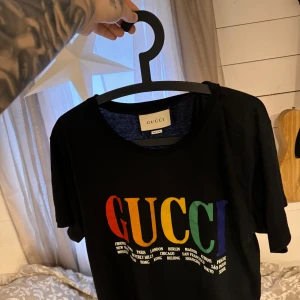 Svart t-shirt från Gucci med regnbågsfärgad text - Säljer denna t-shirt från Gucci (strlk M) då jag ej har användning för den längre. Hör av er vid intresse, säljer de flesta märkeskläder jag äger då det inte tilltalar mig längre 