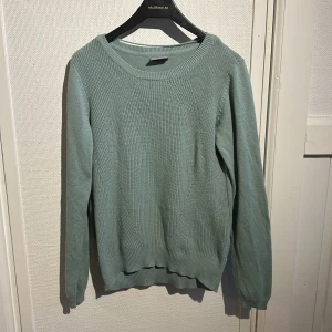 Grön stickad tröja från Vero Moda - Säljer en stilren grön stickad tröja från Vero Moda. Tröjan har en rund halsringning och långa ärmar, perfekt för kyligare dagar. Den är mjuk och bekväm med ribbade detaljer vid ärmslut och nederkant. Lite nopprig i armhålan. 