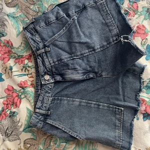 Blå jeansshorts från Never Denim - Säljer ett par snygga blå jeansshorts från Never Denim för att de är för stora för mig. De har en fransig kant och klassisk femficksdesign. Jag skulle uppskatta att det är storlek 36 men kan även fungera för 34 beroende på hur tajt man vill ha de. 
