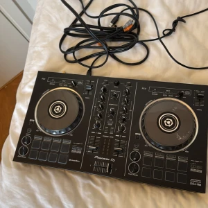 Svart DJ-kontroller från Pioneer DJ - Säljer en svart DJ-kontroller, modell DDJ-RB, från Pioneer DJ. Den har två joghjul, flera reglage och knappar för mixning och effekter. Perfekt för både nybörjare och erfarna DJs som vill ha en kompakt och portabel lösning. Inkluderar kablar för anslutning. App heter rekordbox 
