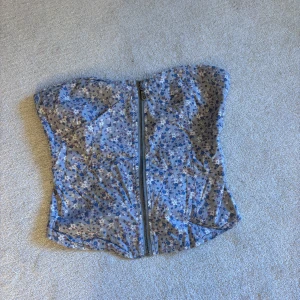 Blommig korsettopp från Orsay - Säljer en söt blommig korsettopp från Orsay med dragkedja framtill. Toppen har ett elastiskt parti på baksidan för bättre passform. Perfekt för sommarens varma dagar! Ej struken just nu. Säljer pågrund av flytt och för mycket kläder 😇😇