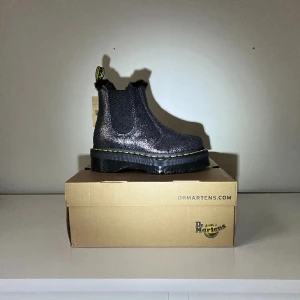 Svarta och silver Chelsea boots från Dr. Martens - Oanvända platform Chelsea boots från Dr. Martens i en glittrig svart färg. Skorna har en robust sula och är fodrade. Perfekta nu i det kalla vädret. Säljer då det tyvär är försmå för mig 🫤⛄️nypris: 2500 modell: 2976 quadfl
