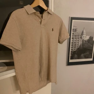 Beige pikétröja från Ralph Lauren - Säljer en stilren beige pikétröja från Ralph Lauren i slim fit. Tröjan har korta ärmar och en klassisk krage med knappar. Perfekt för en avslappnad men ändå elegant look.