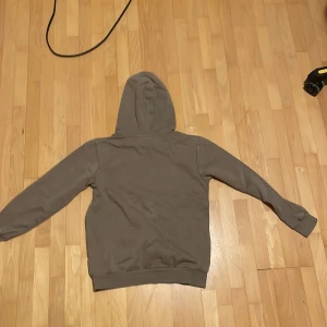 Grå hoodie från Kappahl - Säljer en grå hoodie från Kappahl med texten 'California West Coast' på framsidan. Tröjan har en klassisk design med huva och långa ärmar. Perfekt för en avslappnad stil.