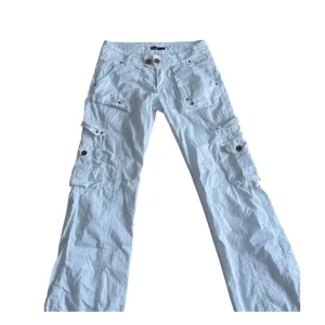 Vita cargopants med fickor🤍 - Snygga vita cargopants med flera praktiska fickor och knappar. Perfekta för en avslappnad stil. Byxorna har en rak passform jätte fint på kroppen (bilder på finns fråga pm). En knappt saknas på baksidan men den förstör inte användningen (se sista bilden) Mått, midjemått: 40cm. Innebenslängd: 79cm. Skriv vid frågor❕
