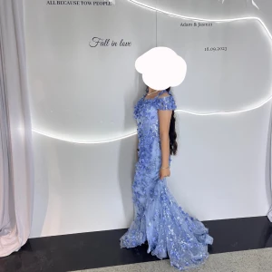 Ljusblå långklänning med blommiga detaljer - Elegant ljusblå långklänning med blommiga applikationer och offshoulder-design. Klänningen har en figursydd passform och är perfekt för speciella tillfällen. Den har en vacker slits och är dekorerad med spetsdetaljer.