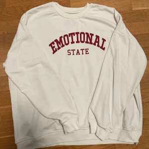 Vit sweatshirt med tryck - Säljer en vit sweatshirt med texten 'Emotional State' i rött på bröstet. Tröjan har en klassisk rund hals och långa ärmar med ribbade muddar vid ärmslut och nederkant. 💖✨