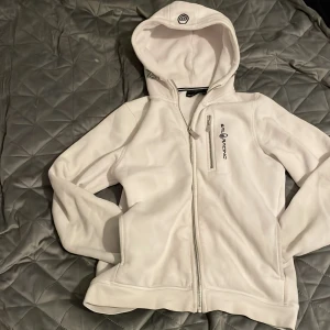 Vit fleecejacka från Sail Racing - Säljer en vit fleecejacka från Sail Racing med dragkedja och broderad logga. Jackan har en huva och en bröstficka med dragkedja. Perfekt för kyliga dagar!