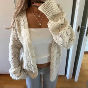 Beige stickad kofta - Mysig beige stickad kofta med knappar framtill. Perfekt för kyligare dagar och lätt att matcha med olika outfits. Koftan har ett fint mönster och långa ärmar som ger en avslappnad look. 