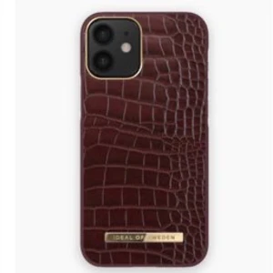 Rött mobilskal från Ideal of Sweden - Snyggt mobilskal i röd färg med krokodilpräglat mönster från Ideal of Sweden. Skalet har en elegant design med en guldig detalj längst ner. Perfekt för att ge din telefon ett stilrent och lyxigt utseende.