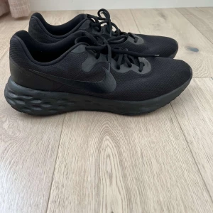 Svarta sneakers  - Säljer ett par svarta Nike sneakers i nyskick. De har en stilren design med snörning och en bekväm sula som passar perfekt för träning eller vardagsbruk. Skorna är helt svarta vilket gör dem lätta att matcha med olika outfits.