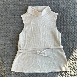 Beige ärmlös polotopp från Zara - Säljer denna as snygga beigea ärmlösa polotopp från Zara. Toppen har en ribbad struktur och ett knytband i midjan för en snygg passform. Perfekt för både vardag och festliga tillfällen!