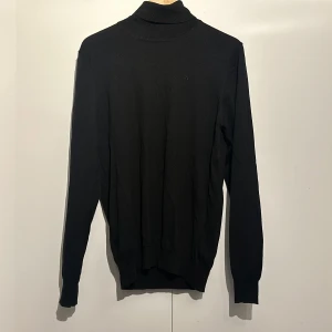 Svart polotröja från J.Lindeberg - Säljer en stilren svart polotröja från J.Lindeberg. Den är gjord i 100% merinoull vilket gör den supermjuk och perfekt för kyligare dagar. Tröjan har långa ärmar och en klassisk passform. Perfekt för både vardag och fest!