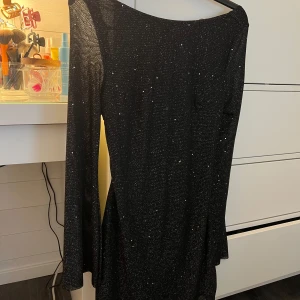 Svart glittrig klänning - Säljer en superfin svart klänning med glittriga detaljer från Shein. Den har en öppen rygg med knytband och långa ärmar. Klänningen har prislappen kvar och är aldrig använd. Perfekt för fest eller nyår! ✨