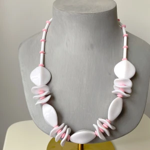 Vitt och rosa halsband med unika former - Säljer ett supercoolt plasthalsband i vitt och rosa. Det har stora, ovala pärlor i vitt och små, runda rosa pärlor som ger en fin kontrast. Perfekt för att piffa upp en outfit med sin unika design och färgkombination. Passar både till vardags och fest!