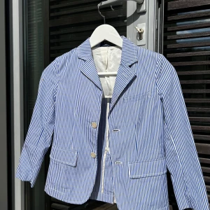 Ralph Lauren barnkavaj 7 år  - Jättefin vit och blå randig Ralph Lauren kavaj. Kavajen är ofodrad med bara ett slag / ok på insidan över axlarna. Mycket fin och knappt använt. Köpt på Ralph Lauren på NK för 2995 kr