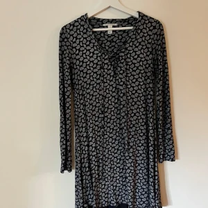 Svart mönstrad klänning från NLY Trend - Säljer en superfin svart klänning från NLY Trend med ett vitt paisleymönster. Klänningen har långa ärmar och en söt knytning framtill. Perfekt för både vardag och fest! Materialet är mjukt och skönt, gjort av viskos och elastan.
