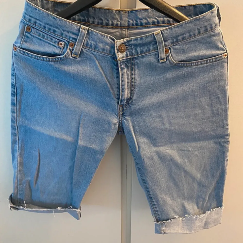 Säljer ett par klassiska jeansshorts från Levi Strauss & Co. i ljusblå denim. De har en normal passform med fem fickor och knappar framtill. Shortsen har en snygg uppvikt kant vid benen och är perfekta för en avslappnad sommarstil.. Shorts.