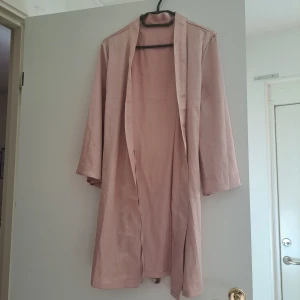 Beige omlottjacka med knytband - Säljer en superfin champagne satin morgonrock. Det är i ett mjukt och bekvämt material, vilket gör den både stilren och skön att bära. Perfekt för en avslappnad men chic look! Använt 1 gång bara.