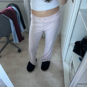 Ljusrosa mjukisbyxor - Säljer ett par superbekväma ljusrosa mjukisbyxor. De är perfekta för en chill dag hemma eller när du bara vill vara bekväm. Byxorna har en normal passform och är gjorda av mjukt material som känns skönt mot huden. De har en elastisk midja med knappar för extra stil.