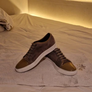 Lanvin skor - Säljer ett par snygga sneakers från Lanvin i grå mocka med en glansig beige cap-toe. Skorna har en vit sula och snörning i matchande färg. Bara att höra av sig vid fundering eller prisförslag