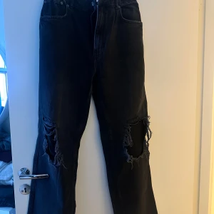 Svarta jeans med slitningar - Säljer ett par svarta baggy jeans med coola slitningar på knäna. De har en straight passform och är perfekta för en avslappnad look. Jeansen är i bra skick och har en snygg, mörk färg som passar till det mesta.
