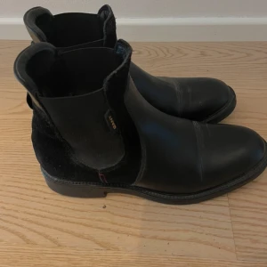 Svarta boots från Gant - Säljer ett par stilrena svarta boots från Gant i skinn och mocka. De har en klassisk design med elastiska paneler på sidorna för enkel på- och avtagning. Perfekta för höst och vinter, dessa boots är både snygga och praktiska.