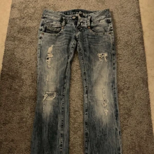 Blåa bootcut jeans med hål - Säljer ett par jättefina lågmidjade blåa jeans med hål. De är i bootcut modell. Köpte här på plick men passade inte mig. De är i bra skick. Står att de är i storlek 25/32 men skulle säga att de är lite större så kontakta gärna om du vill  ha mer exakta mått.
