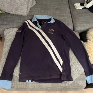 Mörkblå pikétröja från Morris - Säljer en snygg mörkblå pikétröja från Morris med ljusblå krage och manschetter. Väldigt schysst tröja som tyvärr har legat i en låda mestadels. 