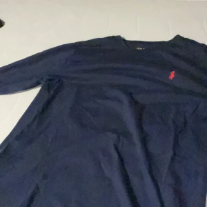 Mörkblå tröja från Polo Ralph Lauren - Säljer en snygg mörkblå tröja från Polo Ralph Lauren. Den har en klassisk design med det ikoniska röda logotypen broderad på bröstet. Perfekt för både vardag och lite finare tillfällen. Tröjan är i bra skick och gjord av mjukt bomullsmaterial. Ordinare pris 800kr