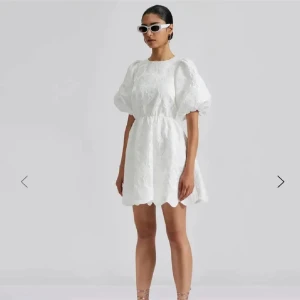 Vit klänning med puffärmar - by malina klänning - Säljer en superfin vit klänning med puffiga kortärmar och en snygg öppen rygg. Den har ett blommigt mönster och är gjord i ett lätt och luftigt material. Klänningen är kort och har en lös passform som ger en avslappnad men chic look.