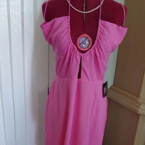 Rosa balklänning från NELLY, stl.40 - Nyskick/oanvänd - Slutsåld/gått ur sortiment. Med originella lappar. Free spirit dress. Maxi längd. Balklänning. Ej stretch. Tunn & skön. Figursydd passform upptill med bredare kjoldel. Öppen rygg med snörning. Snörning runt halsen.  Djup urringning. Slits på vänster sida ben. Dold dragkedja med hyska baktill. Stl: 40. 100% polyester. Mycket behagligt material! Byst: cm Midja: cm Höfter: cm Längd: cm Nypris: 925 kr