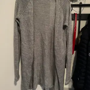 Mysig grå stickad kofta perfekt för kyliga dagar. Den har en enkel design utan knappar och långa ärmar, vilket gör den lätt att matcha med olika outfits. Perfekt för både höst och vinter. Förekommer endel noppor!