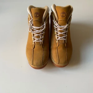 Bruna boots från Timberland - Säljer ett par klassiska bruna Timberland boots i mycket bra skick. De har en robust sula och snörning framtill. Perfekta för höst och vinter med sin slitstarka design och bekväma passform. Skorna har en snygg kontrast med vita detaljer runt ankeln.