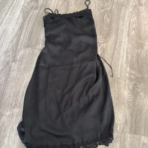 Svart axelbandslös klänning - Snygg svart axelbandslös klänning med spetsdetaljer. Perfekt för en utekväll eller fest. Klänningen har en kort längd och är gjord i ett mjukt material som ger en bekväm passform.