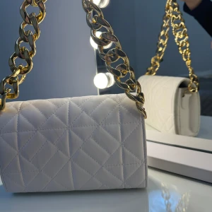Vit quiltad axelväska med guldkedja - Säljer en superfin vit quiltad axelväska. Väskan är i mycket bra skick och passar både till vardags och fest. Den har en stilren design som gör den lätt att matcha med olika stilar. Väskan är helt ny och har aldrig använt den. Priset kan diskuteras