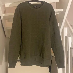 Olivgrön tröja från Smog - Säljer en olivgrön tröja från Smog i storlek L. Tröjan har ett snyggt rutmönster och är perfekt för både höst och vinter. Den är långärmad och gjord i ett bekvämt material som håller dig varm. Passar bra till både vardag och lite mer avslappnade tillfällen.