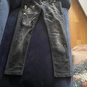 Säljer ett par svarta jeans från Dsquared2 i storlek 44. De har en cool, sliten look med detaljer som slitningar och färgstänk. Perfekta för en avslappnad och trendig stil. Passar bra till både vardag och fest!