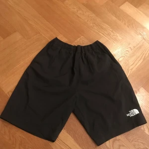 Svarta shorts från The North Face - Säljer ett par svarta shorts från The North Face i storlek M för barn. De är tillverkade i ett snabbtorkande material med FlashDry-teknologi, perfekt för träning eller sommaraktiviteter. Shortsen har en elastisk midja för en bekväm passform.