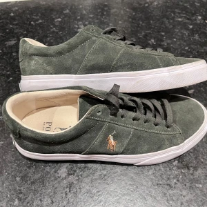 Gröna mocka sneakers från Ralph Lauren - Säljer ett par snygga gröna sneakers från Ralph Lauren i storlek 40. Skorna är i mocka  med en vit sula och har den klassiska Polo-loggan på sidan. Perfekta för både vardag och fest! De är i mycket bra skick och kommer i originalkartong.