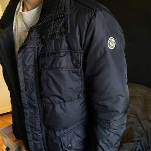 Säljer en snygg marinblå Moncler jacka i mycket bra skick. Den har en quiltad design med dragkedja och knappar, samt flera praktiska fickor. Perfekt för höst och vinter! Säljer den för lite billigare pris för att på dragkedjan har en sak lossnat. Storlek 3 som motsvarar storlek M✅.Köpt på NK i Göteborg, NK påsen följer med och digitalt kvitto kan hittas vid förfrågan✅Priser är inte hugget i sten 🪨 Bara att skriva vid minsta fundering!