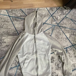 Nike tech tracksuit storlek M pris kan diskuteras  - Säljer en grå hoodie från Nike i bra skick. Den har en dragkedja framtill och en praktisk huva. Perfekt för höst och vår, och funkar lika bra till träning som till vardags. Stor Nike-logga på bröstet ger en sportig look. Skön och bekväm att ha på sig!