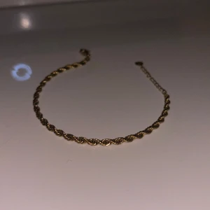 Guldarmband med tvinnad design - Säljer ett elegant guldarmband med en snygg tvinnad design. Perfekt för både vardag och festliga tillfällen. Armbandet är justerbart och passar de flesta handleder. Enkelt men stilrent smycke som ger en touch av lyx till din outfit.