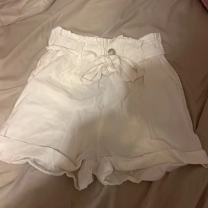 Vita shorts från Amisu - Säljer ett par vita shorts från New yorker i storlek 38. De är högmidjade med ett knytband i midjan för extra stil. 
