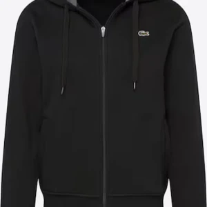 Lacoste zip - Säljer en svart hoodie från Lacoste i bra skick. Den har en dragkedja framtill och en klassisk krokodil-logga på bröstet. Insidan av huvan är grå, vilket ger en snygg kontrast. Perfekt för höst och vår, och funkar både till vardags och chillkvällar. Passar bra till jeans eller joggers!