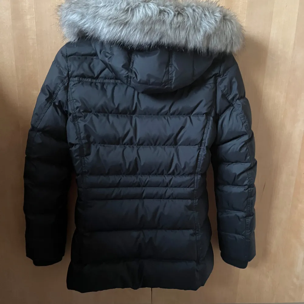 Säljer en snygg svart dunjacka från Tommy Hilfiger i mycket bra skick. Jackan har en avtagbar huva med grå fuskpäls och stängs med dragkedja och knappar. Perfekt för kalla vinterdagar! 🖤. Takit.