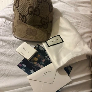 Beige keps från Gucci - Snygg beige keps från Gucci med det ikoniska GG-mönstret. Kepsen har en klassisk design med böjd skärm och justerbart band baktill för perfekt passform. Perfekt för att ge din outfit en lyxig touch.