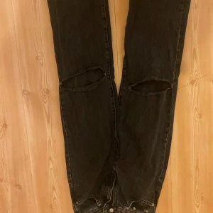 Svarta jeans med slitningar från 157 - Snygga svarta jeans från 157 med coola slitningar vid knäna. Perfekta för en avslappnad och trendig look. De har en klassisk femficksdesign och knappgylf.